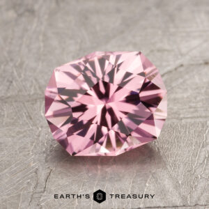 A faceted pink gemstone named ET1609 is displayed on a gray textured background, with the text "Earth's Treasury" elegantly inscribed.