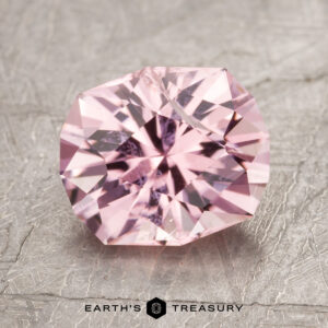 A vibrantly faceted, pink gemstone rests elegantly on a textured grey surface, with the text "Earth's Treasury ET1613" displayed at the bottom of the image.