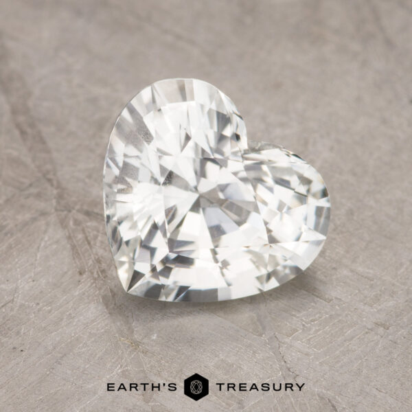 A heart-shaped, faceted 1.93-carat sapphire displayed on a textured surface with the text "EARTH'S TREASURY" at the bottom.