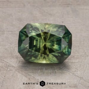 A 2.15-carat Australian sapphire, rectangular cut with multicolored green and yellow hues, placed on a textured surface featuring the "Earth's Treasury" logo at the bottom.