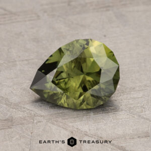 A faceted, pear-shaped 1.65-carat Australian Sapphire sits on a gray textured surface, with the words "EARTH'S TREASURY" at the bottom of the image.