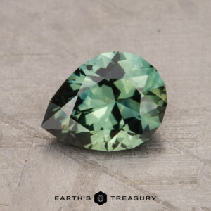 A pear-shaped, green gemstone is displayed on a textured surface. The label "EARTH'S TREASURY" is visible at the bottom of the image, showcasing a 1.60-carat Australian Sapphire.