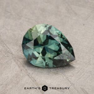 A 1.43-carat Australian sapphire, pear-shaped and green, is showcased on a textured gray surface with the text "Earth's Treasury" at the bottom.