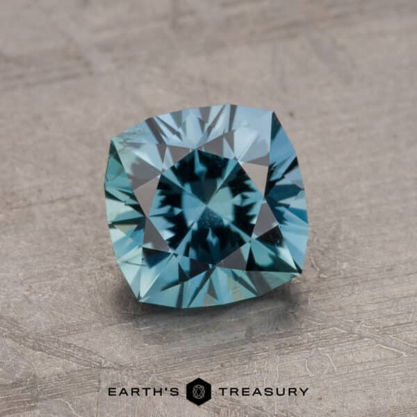 A 1.67-carat Montana Sapphire with a faceted, square cut rests on a textured surface, gleaming in blue hues. The text "Earth's Treasury" is visible at the bottom of the image.