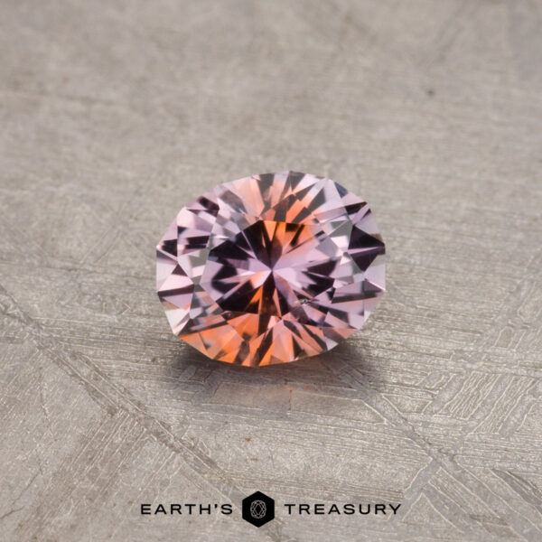 A 0.65-carat Montana sapphire (heated) showcasing a mix of pink and orange hues, resting on a textured surface with the text "Earth's Treasury" at the bottom.