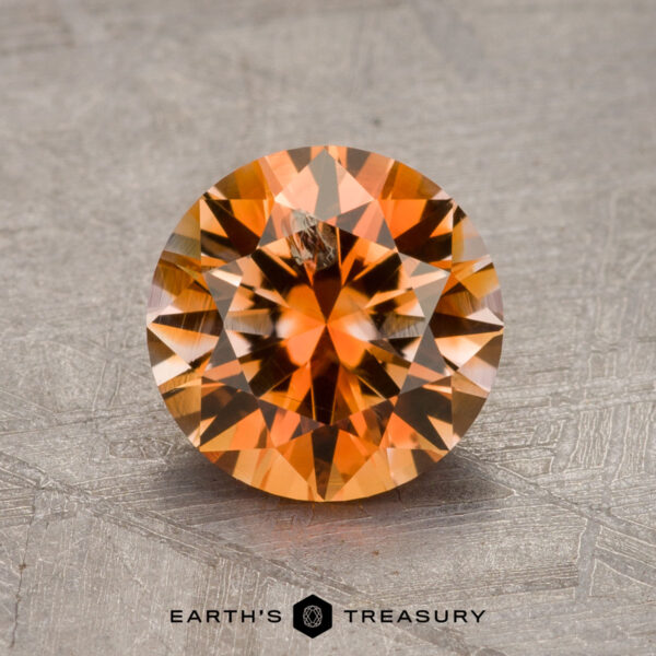 A 1.85-carat faceted orange Montana sapphire sits on a textured surface. The inscription at the bottom reads "Earth's Treasury.