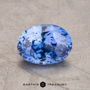 A faceted 2.12-carat oval blue sapphire gemstone displayed on a textured gray background with the logo "EARTH'S TREASURY" at the bottom.