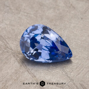 A 1.16-carat pear-shaped sapphire with intricate facets is placed on a textured surface. The name "Earth's Treasury" is visible at the bottom of the image.