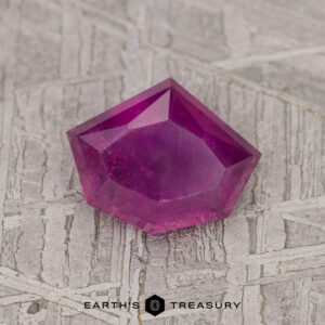 A 1.69-carat rich purple Umba sapphire on a textured surface with the logo and text "Earth's Treasury" below it.