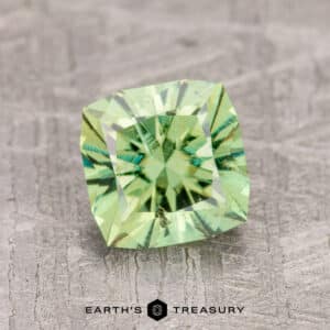 A 1.63-carat Demantoid Garnet, with square cuts and reflective facets, sits on a textured gray surface.