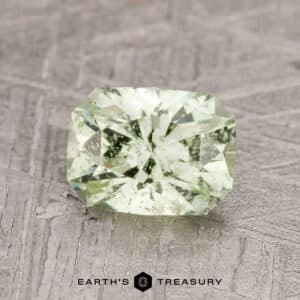 The 1.52-carat pale green grossular garnet, featuring multiple facets, is displayed on a textured gray surface.