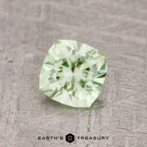 A 0.71-carat mint green garnet with intricate faceting, showcased on a textured gray background. Text reads "Earth's Treasury" at the bottom of the image.