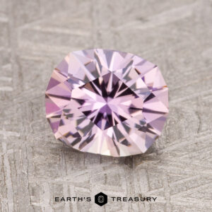 A 1.78-carat Fancy Tanzanite gemstone, round and faceted with a soft lavender hue, is displayed on a textured gray surface.