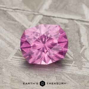 A 1.71-carat pastel pyrope color-change garnet cut in a hexagon shape, resting on a textured gray surface.