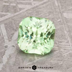 A 1.67-carat mint green grossular garnet with a square cut rests on a textured surface. Text below reads "Earth's Treasury.