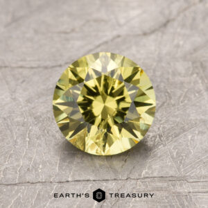 A round brilliant cut yellow gemstone, product ET1087, on a textured gray surface.