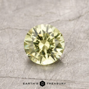 A faceted green gemstone, product ET1090, displayed on a textured gray surface.