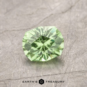 An ET1107, a faceted green gemstone with a geometric pattern, rests on a textured gray surface.