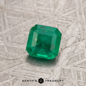 A textured surface showcases a green emerald cut gemstone, with "Earth's Treasury" inscribed below.