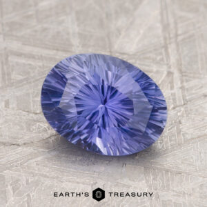 A 1.87-carat Ceylon sapphire, faceted into an oval shape with a stunning radial pattern, sits elegantly on a textured gray surface.