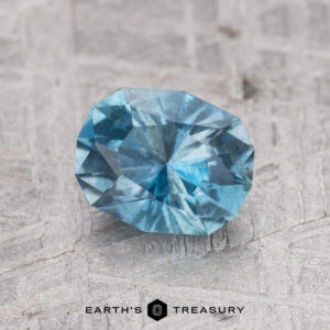 A 1.05-carat Nasarawa Teal Aqua gemstone displayed on a textured surface.