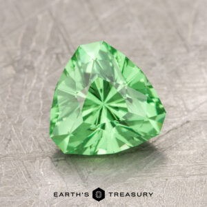 The ET1157 is a gemstone with a green heart shape and facets, elegantly displayed on a textured surface.