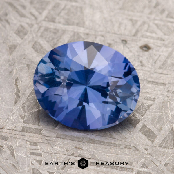 Close-up of a round Violet-Blue Ceylon sapphire gemstone, weighing 1.83 carats, resting on a textured gray surface.