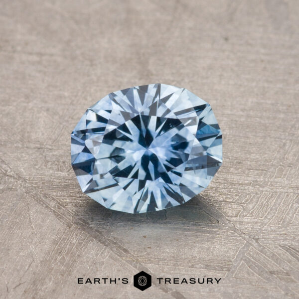 A faceted blue gemstone displayed on a textured surface, with the product name "1.19-Carat Montana Sapphire (Heated)" at the bottom.