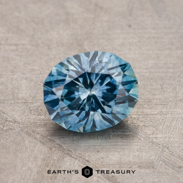 A 1.15-carat heated Montana sapphire with intricate facets lies on a textured surface, showcasing a sparkling pattern.