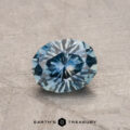 A faceted, round 1.03-carat heated Montana sapphire with a geometric sparkle pattern, placed on a textured gray surface.