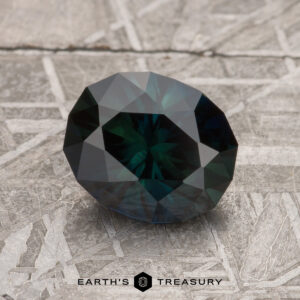 A dark, faceted 1.89-carat Midnight Blue-Green Australian Sapphire, resting on a gray textured surface, with the "Earth's Treasury" logo displayed at the bottom.