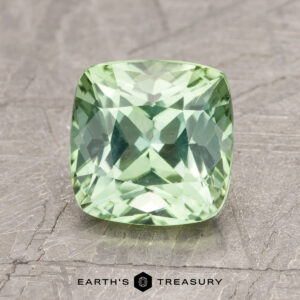 A cushion-cut green gem labeled ET1399 is showcased on a textured surface, with the "Earth's Treasury" logo visible beneath it.