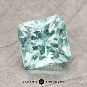 ET1395's square-cut aquamarine gemstone, featuring intricate facets, is placed on a textured surface.