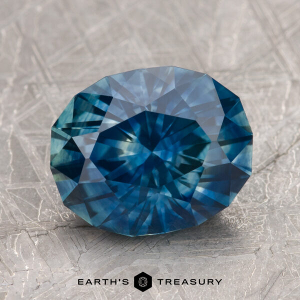 A 3.32-carat Montana sapphire with intricate facets rests on a textured gray surface.