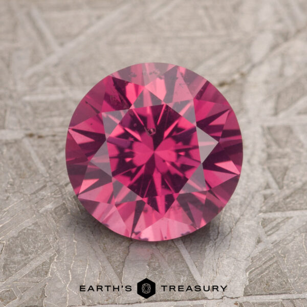 A 2.26-carat magenta pink Burmese spinel with intricate faceting is displayed on a textured gray surface, featuring the logo "Earth's Treasury" beneath it.