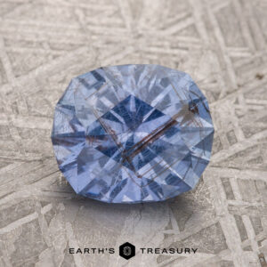 A 2.28-carat violet-blue Umba sapphire with visible inclusions rests on a textured, silver-gray surface.