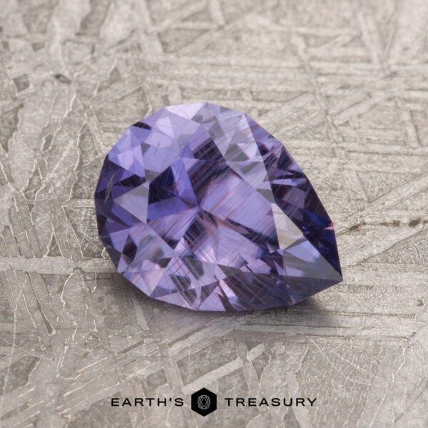 A 1.56-carat, pear-shaped Rich Purple Umba Sapphire rests on a textured surface, with the words "Earth's Treasury" displayed beneath.