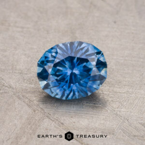 A 0.92-carat Montana Sapphire, heated and faceted in blue, displayed on a textured surface with the "Earth's Treasury" logo at the bottom.