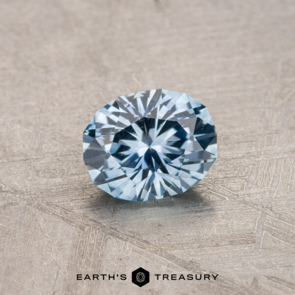 A 0.80-carat Montana sapphire with a heated, faceted round cut is displayed on a textured surface.