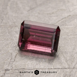 Gemstone ET1434, featuring a rectangular cut in deep pink, is showcased on a textured gray surface with the text "Earth's Treasury" below.