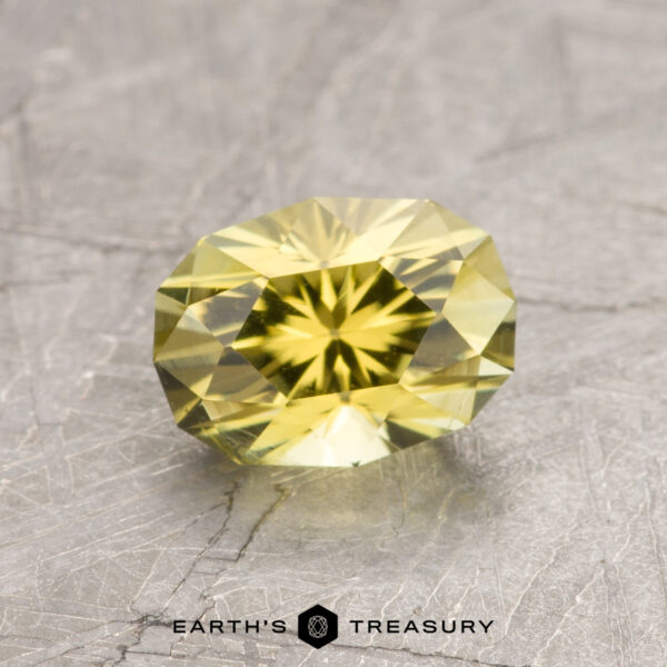 A faceted yellow ET1445 gemstone rests on a textured gray surface, with the words "Earth's Treasury" displayed at the bottom.