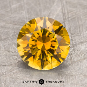 A 2.75-carat golden yellow Montana sapphire with a faceted surface set against a textured silver background, labeled "Earth's Treasury.