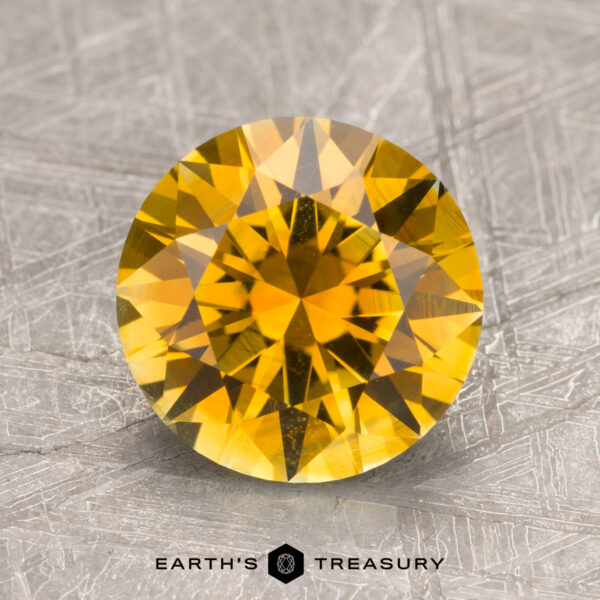 A 2.75-carat golden yellow Montana sapphire with a faceted surface set against a textured silver background, labeled "Earth's Treasury.