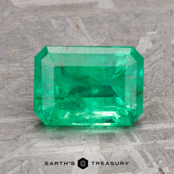 A 2.23-carat Colombian treated emerald resting on a textured gray surface.