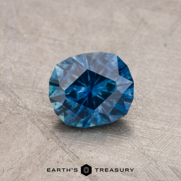 A 1.03-carat Montana sapphire, featuring a rectangular cut with multiple facets, is placed on a textured surface.