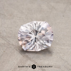 A 1.16-carat Montana sapphire on a textured surface with the logo "Earth's Treasury" underneath.