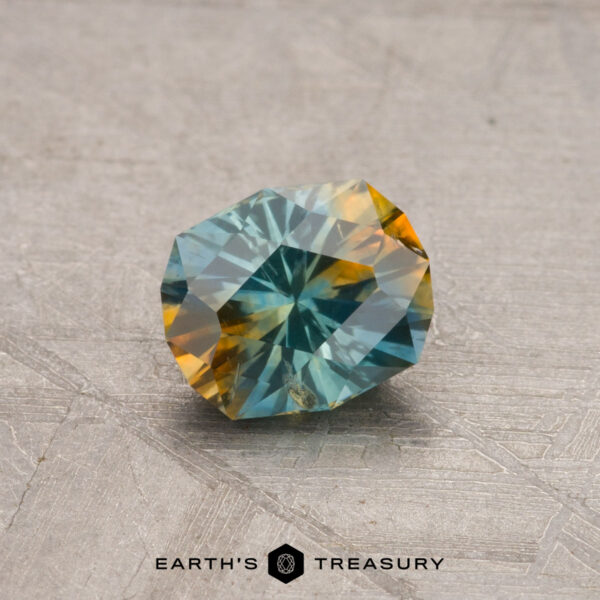 A 0.92-carat heated Montana sapphire, showcasing a blend of blue and orange hues, resting on a textured surface.