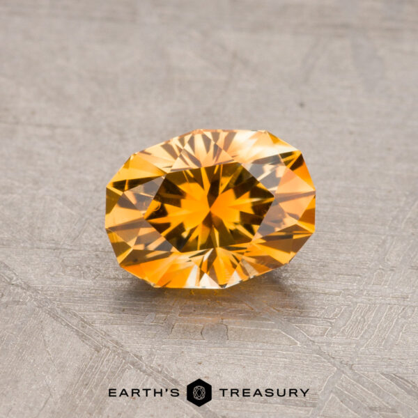 A faceted, oval-cut golden yellow 1.09-carat Montana sapphire (heated) displayed on a textured surface. Logo reads "Earth's Treasury.