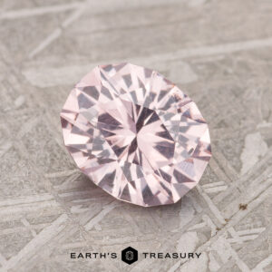 A 1.67-carat pale pink Mahenge garnet with a round faceted cut on a textured gray surface.