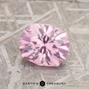 A 1.87-carat Lilac Pink Mahenge Garnet is elegantly showcased on a textured gray surface, with the text "Earth's Treasury" appearing at the bottom.